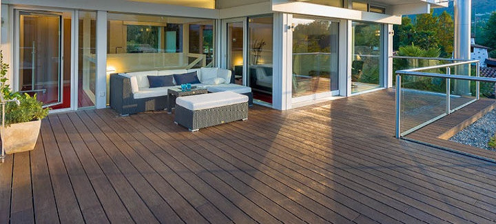 Moderne Terrasse mit dunklem Escheholz-Belag, stilvoller Rattan-Lounge mit weißen Polstern und direktem Zugang zum Wohnbereich.