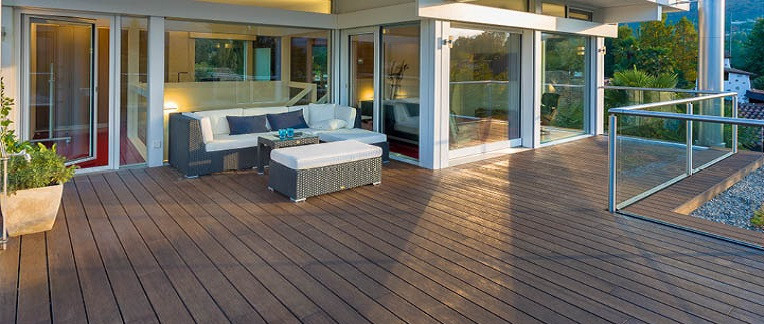 Moderne Terrasse mit dunklem Escheholz-Belag, stilvoller Rattan-Lounge mit weißen Polstern und direktem Zugang zum Wohnbereich.