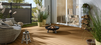 Helle Terrasse vor einem Haus, umgeben von einem Sichtschutzzaun mit dekorativen Elementen.