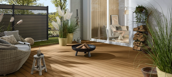 Helle Terrasse vor einem Haus, umgeben von einem Sichtschutzzaun mit dekorativen Elementen.