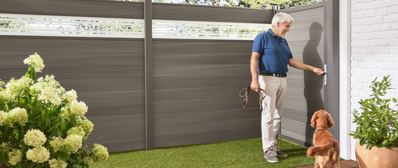  Stilvoller WPC-Sichtschutzzaun im Landhausgarten, kombiniert mit hellen Loungemöbeln und grüner Bepflanzung.