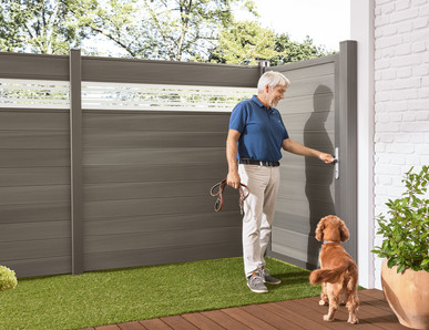  Stilvoller WPC-Sichtschutzzaun im Landhausgarten, kombiniert mit hellen Loungemöbeln und grüner Bepflanzung.