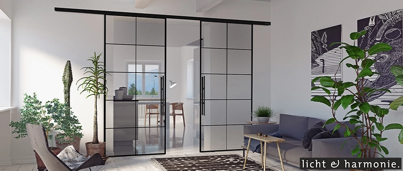 Glas-Schiebetüren mit schwarzem Rahmen als moderner Raumtrenner im Wohnzimmer. Design von licht & harmonie.