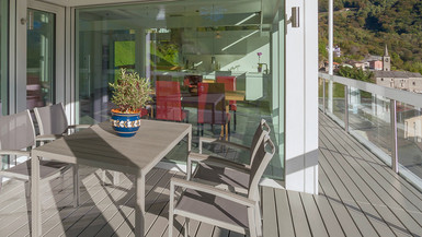 Überdachte Terrasse mit grauem Holzboden, modernem Esstisch-Set und Blick in den offenen Wohnbereich.